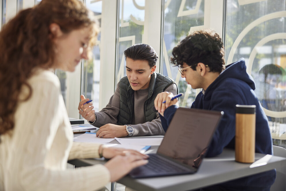 Drei Bachelor-Studierende sitzen im Gruppenraum und arbeiten an ihren Laptops