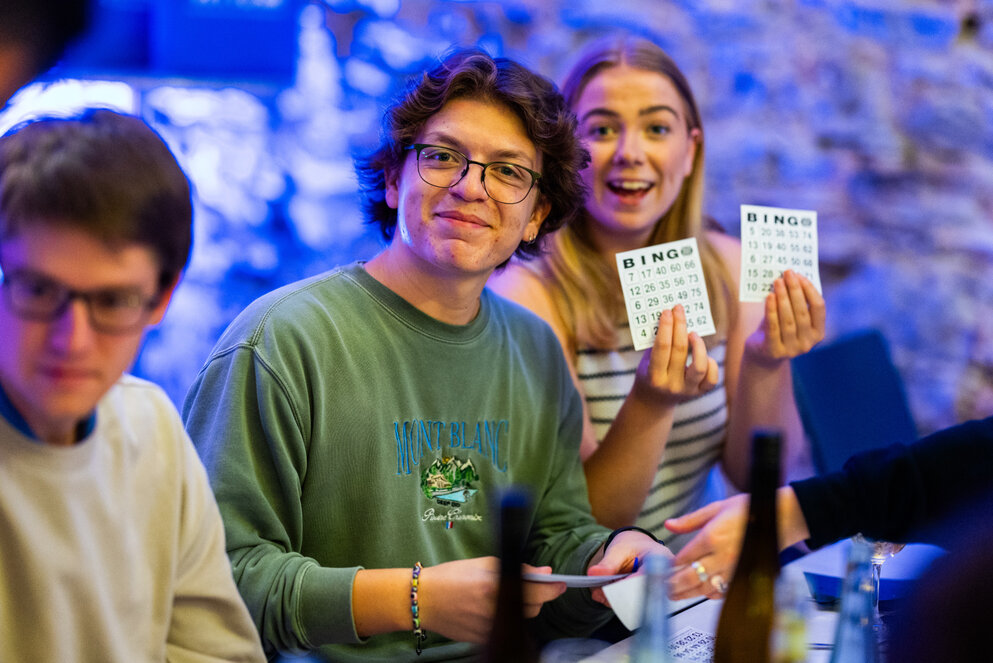 Drei lächelnde WHU Studierende spielen Bingo bei einer Veranstaltung in Vallendar