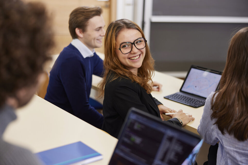 Eine Frau mit Brille lächelt, während sie vor einem Laptop sitzt.
