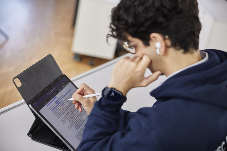 Ein dunkelhaariger Bachelor-Studierende sitzt an einem Schreibtisch und studiert seinen Laptop